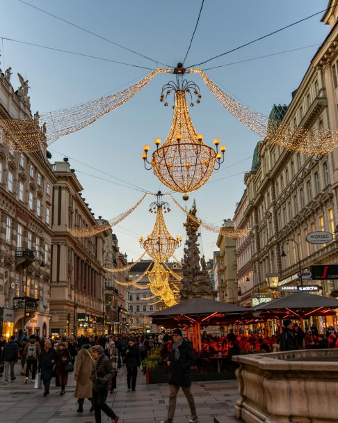 Weihnachtsmarkt in Wien mit festlicher Lichter-Dekoration zwischen den Häusern. Menschen laufen zwischen den Marktständen.